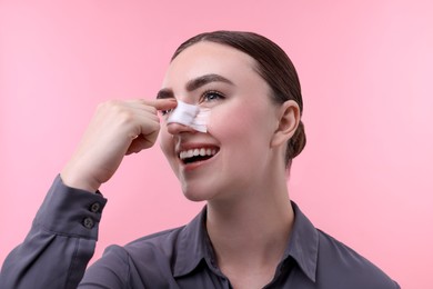 Woman with medical bandage on her nose after plastic surgery operation against pink background