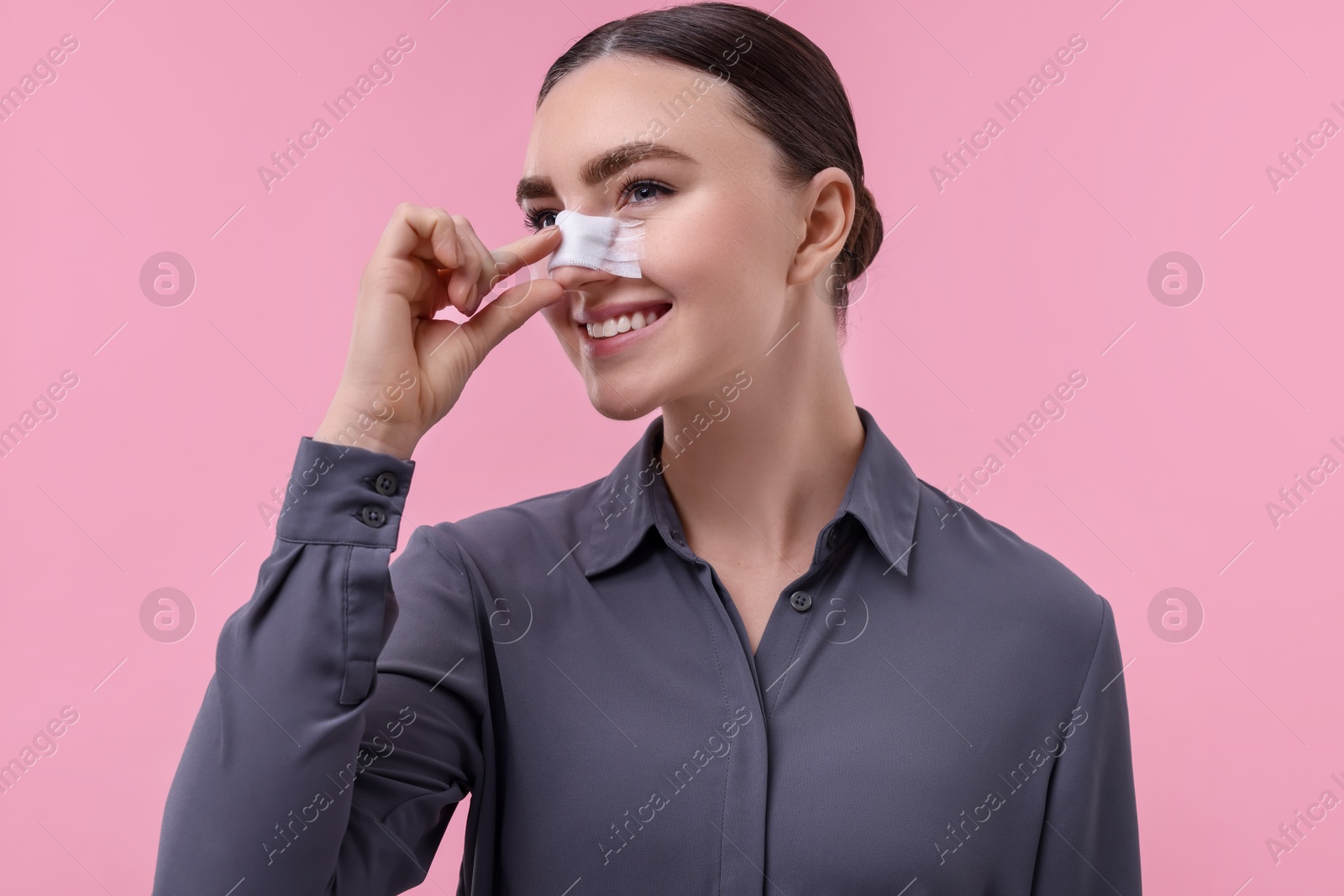 Photo of Woman with medical bandage on her nose after plastic surgery operation against pink background