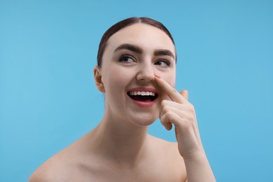 Woman touching her nose on light blue background