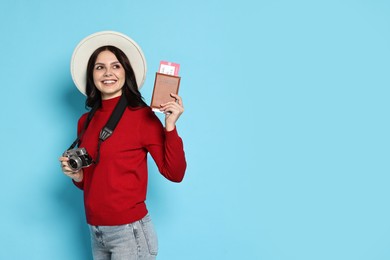 Photo of Young tourist in hat with camera, passport and tickets on light blue background, space for text