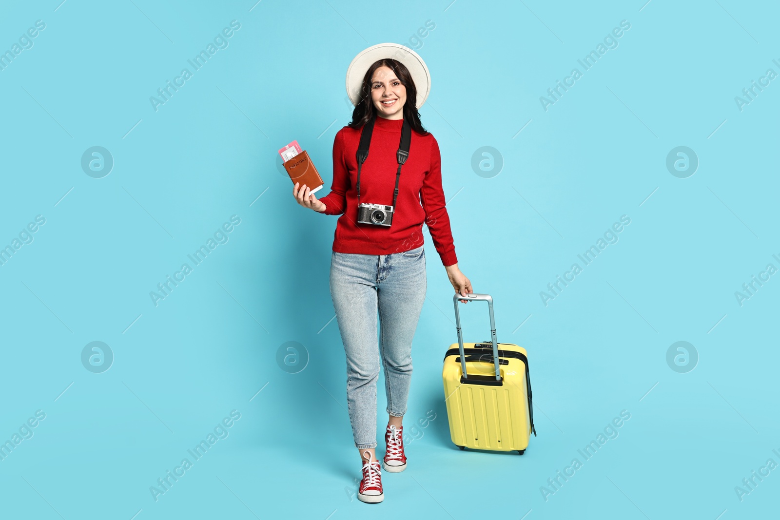 Photo of Young tourist in hat with camera, passport, tickets and suitcase on light blue background