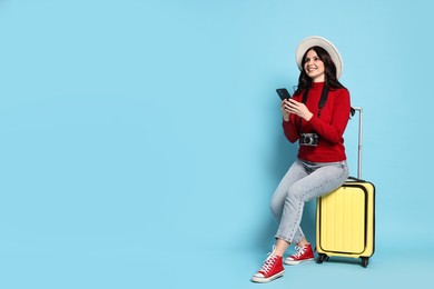 Photo of Young tourist in hat with camera, phone and suitcase on light blue background, space for text