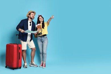 Tourism. Happy couple with map and suitcase on light blue background, space for text