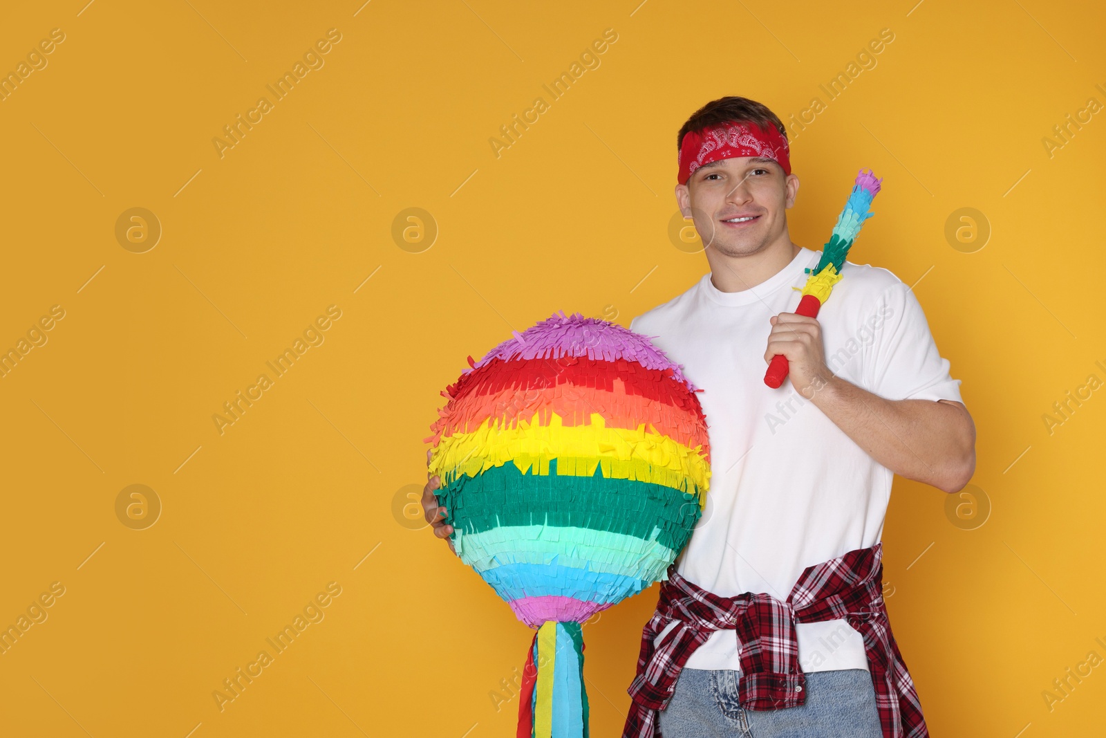 Photo of Happy man with colorful pinata and stick on yellow background. Space for text