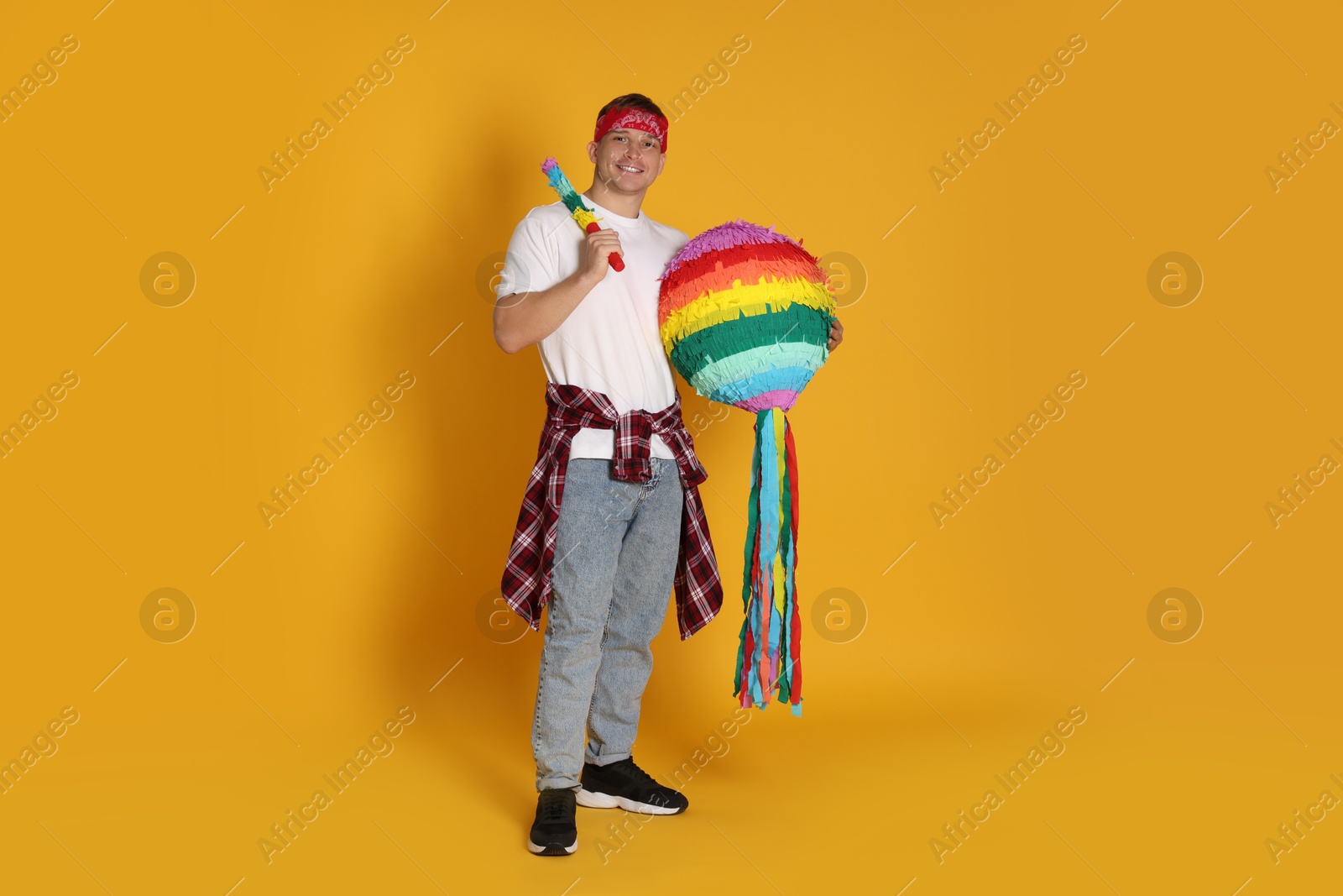 Photo of Happy man with colorful pinata and stick on yellow background