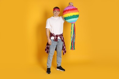 Photo of Happy man with colorful pinata on yellow background