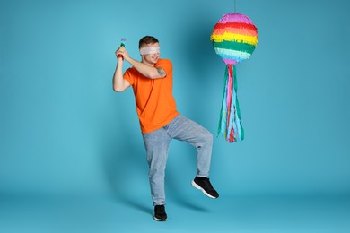 Photo of Man with tied eyes breaking pinata on light blue background