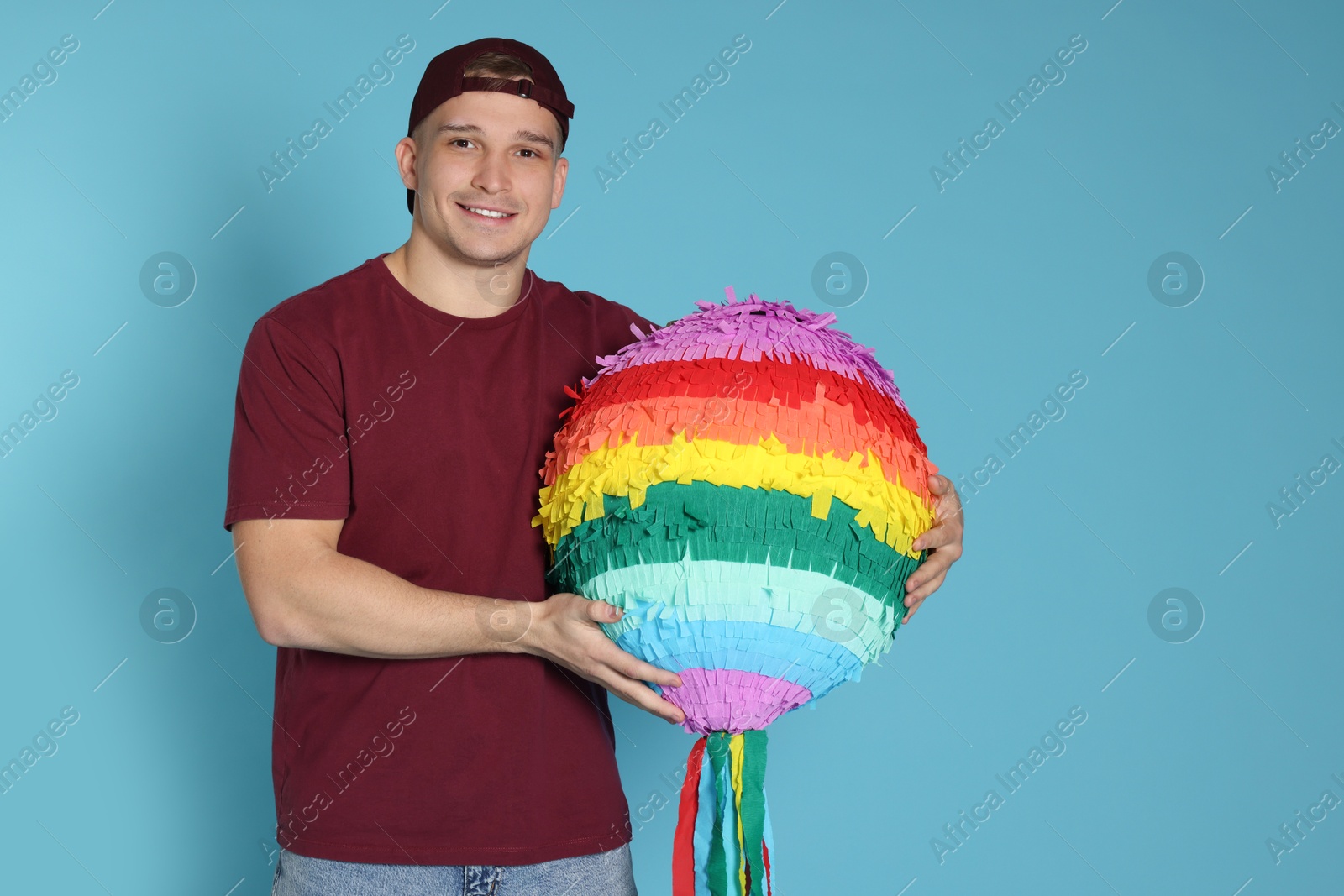 Photo of Happy man with colorful pinata on light blue background. Space for text