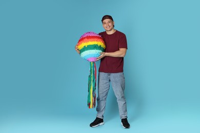 Happy man with colorful pinata on light blue background