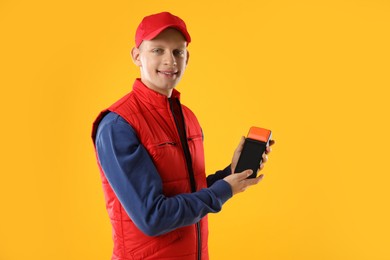 Happy courier with payment terminal on yellow background