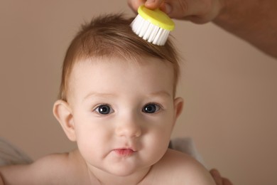 Photo of Man brushing hair of his little baby on dark beige background, closeup