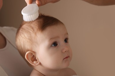 Photo of Parents brushing hair of their little baby on dark beige background, closeup. Space for text