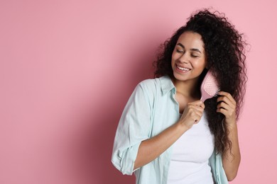 Smiling young woman brushing her curly hair on pink background, space for text