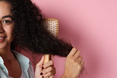 Photo of Woman brushing her curly hair on pink background, closeup