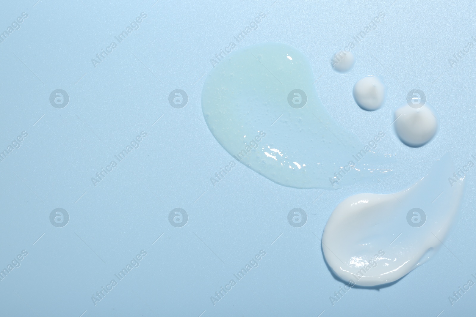 Photo of Cream and gel samples on light blue background, top view. Space for text