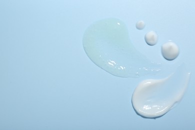 Photo of Cream and gel samples on light blue background, top view. Space for text