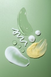 Photo of Cream and gel samples on green background, top view