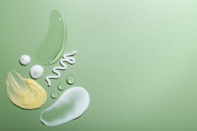 Photo of Cream and gel samples on green background, top view. Space for text