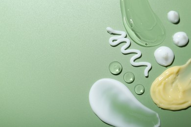 Photo of Cream and gel samples on green background, top view. Space for text