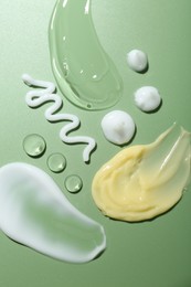 Photo of Cream and gel samples on green background, top view