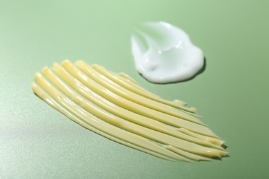 Photo of Cream samples on green background, closeup. Skincare product