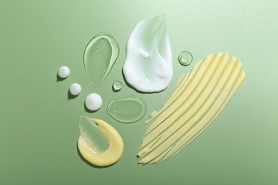 Photo of Cream and gel samples on green background, top view