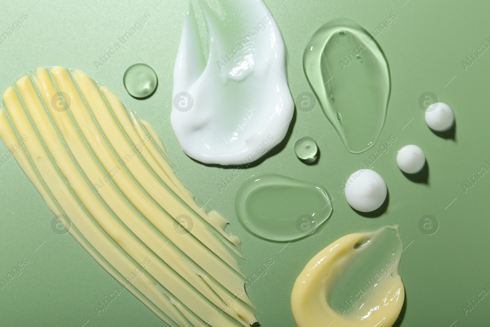 Photo of Cream and gel samples on green background, top view