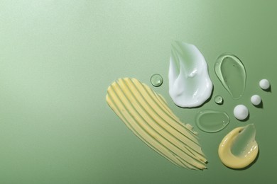 Photo of Cream and gel samples on green background, top view. Space for text