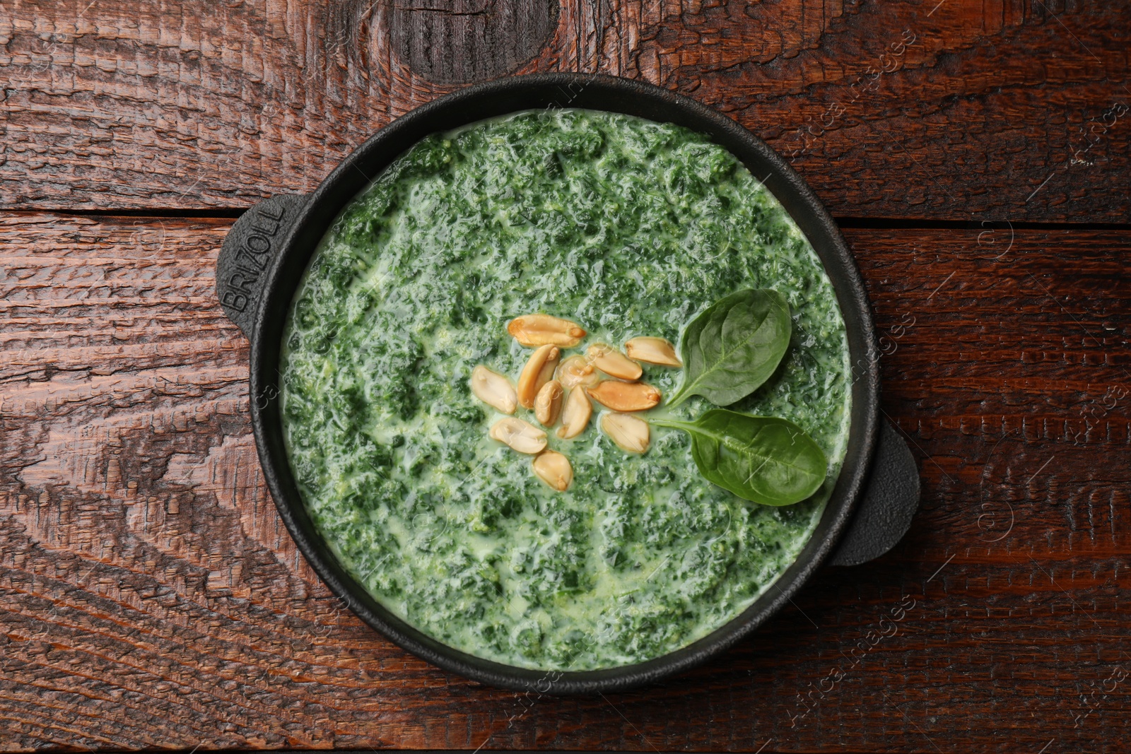 Photo of Delicious spinach sauce with peanuts on wooden table, top view