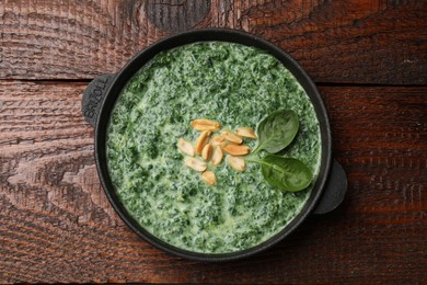 Photo of Delicious spinach sauce with peanuts on wooden table, top view