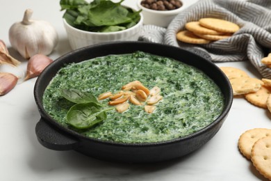 Photo of Delicious spinach sauce with peanuts and crackers on white table, closeup