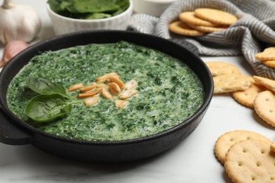 Photo of Delicious spinach sauce with peanuts and crackers on white table, closeup