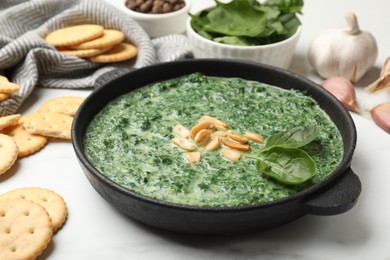 Photo of Delicious spinach sauce with peanuts and crackers on white table, closeup