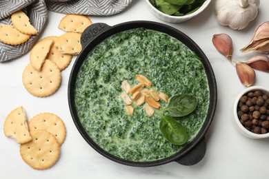 Photo of Delicious spinach sauce with peanuts and crackers on white table, flat lay