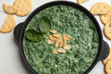 Photo of Delicious spinach sauce with peanuts and crackers on white table, flat lay