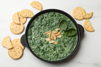 Photo of Delicious spinach sauce with peanuts and crackers on white table, flat lay