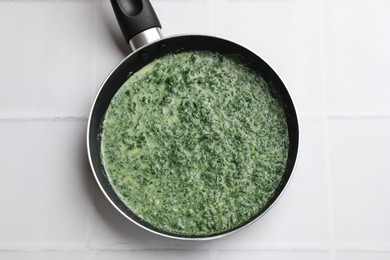 Photo of Delicious spinach sauce on white tiled table, top view