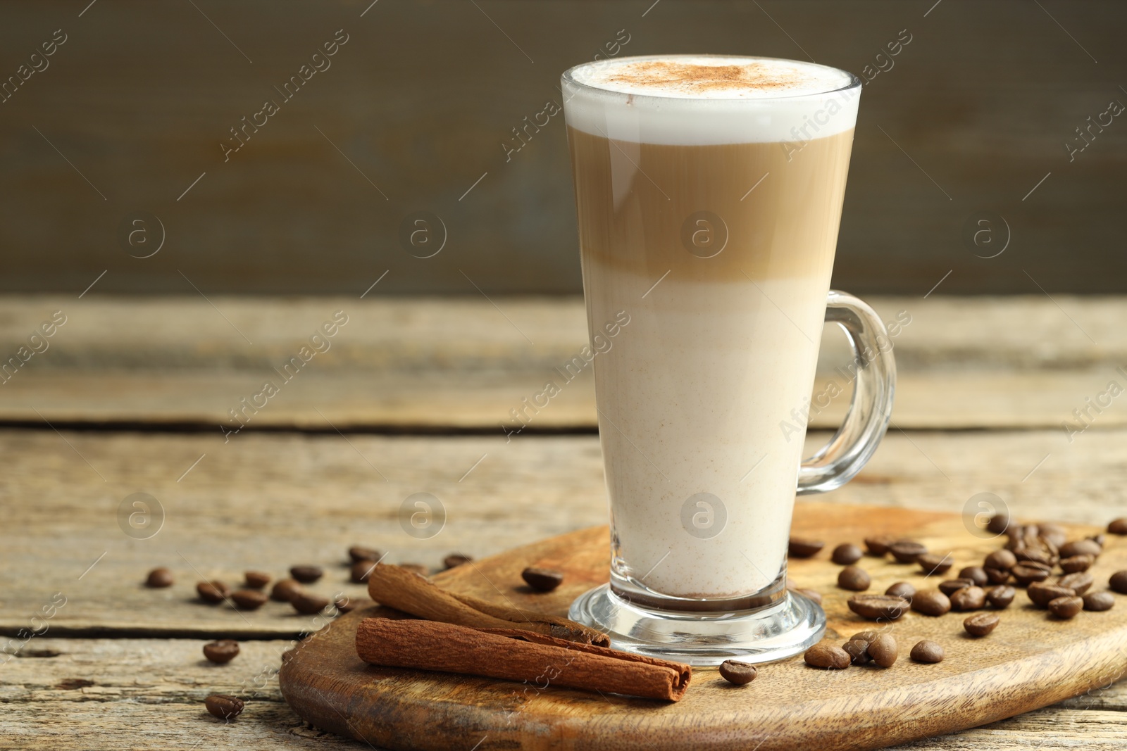 Photo of Tasty latte macchiato in glass cup, coffee beans and cinnamon on wooden table, closeup. Space for text