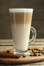 Photo of Tasty latte macchiato in glass cup, coffee beans and cinnamon on wooden table, closeup