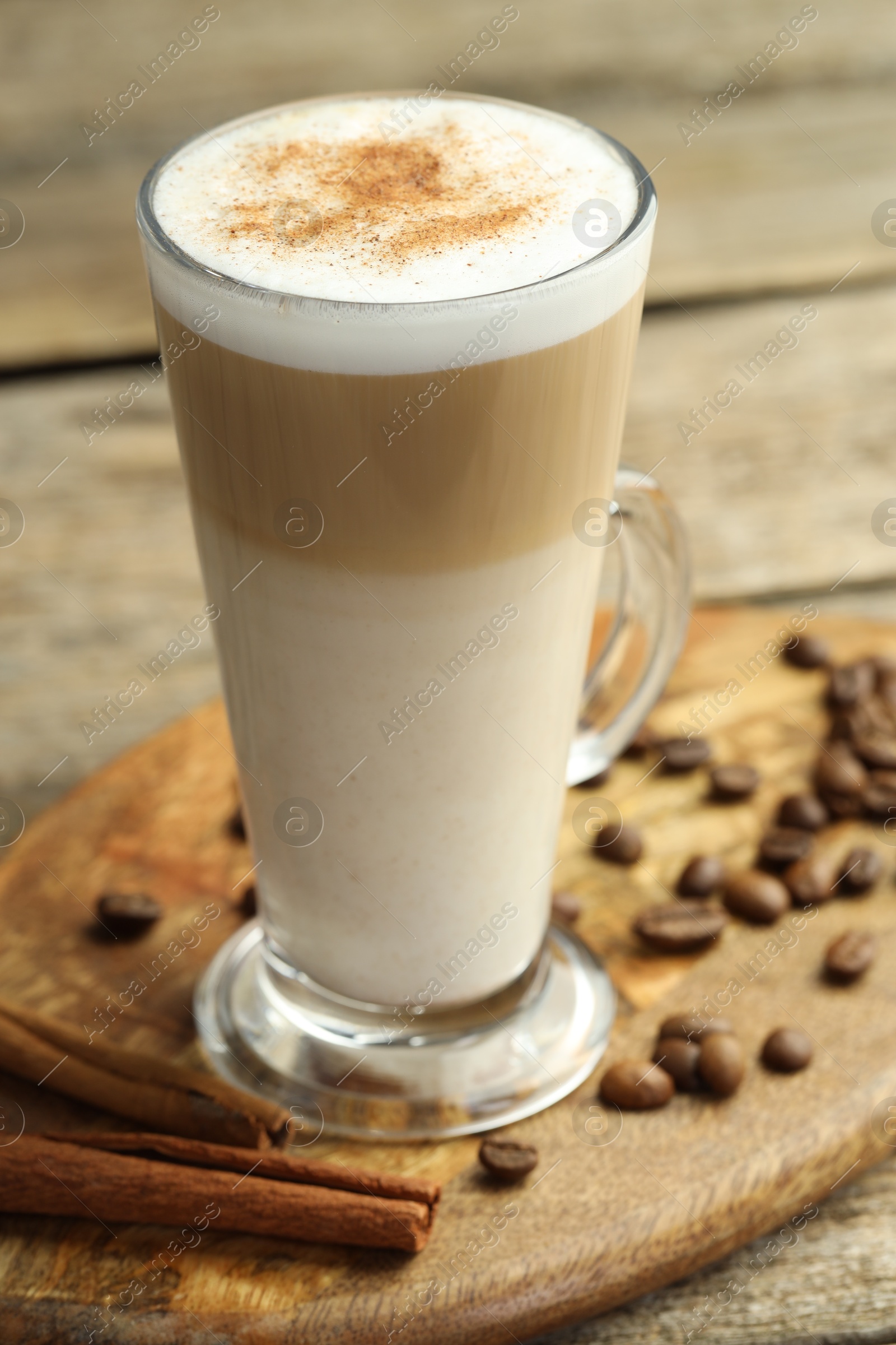 Photo of Tasty latte macchiato in glass cup, coffee beans and cinnamon on wooden table, closeup