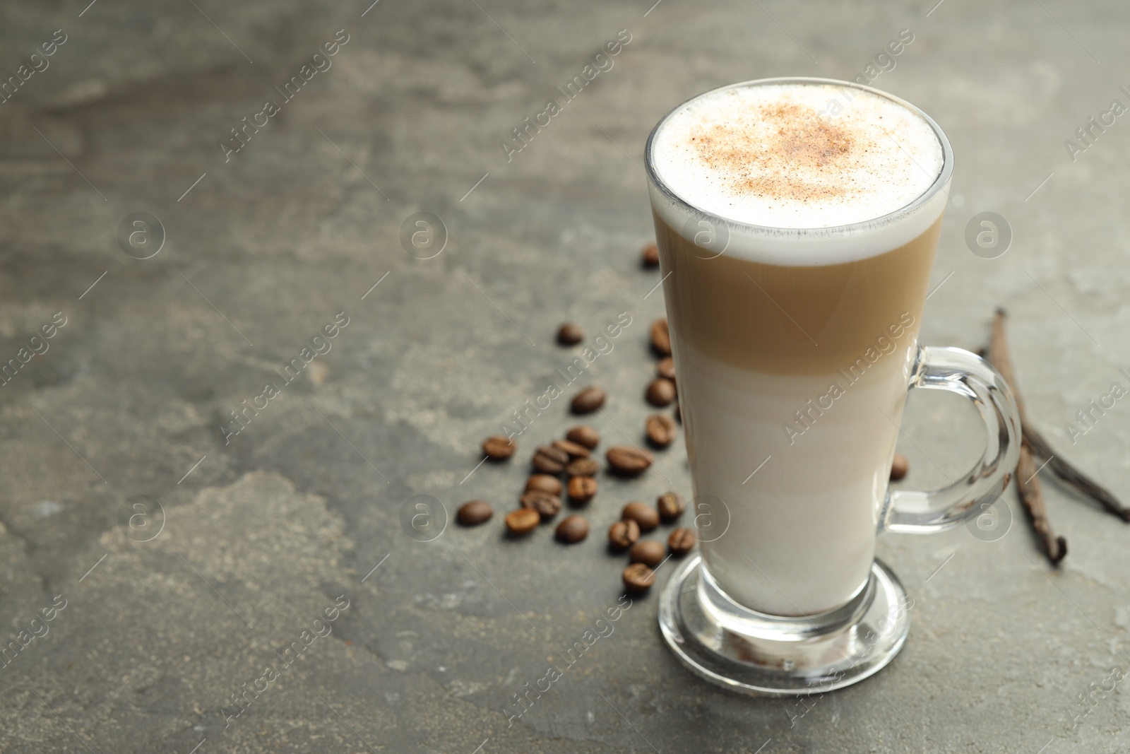 Photo of Tasty latte macchiato in glass cup, coffee beans and vanilla pods on grey table, closeup. Space for text