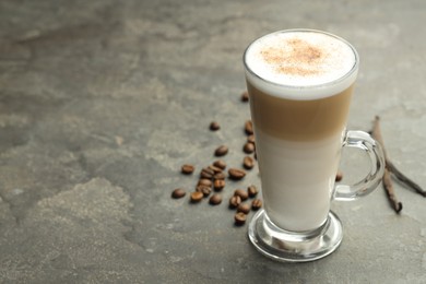 Photo of Tasty latte macchiato in glass cup, coffee beans and vanilla pods on grey table, closeup. Space for text