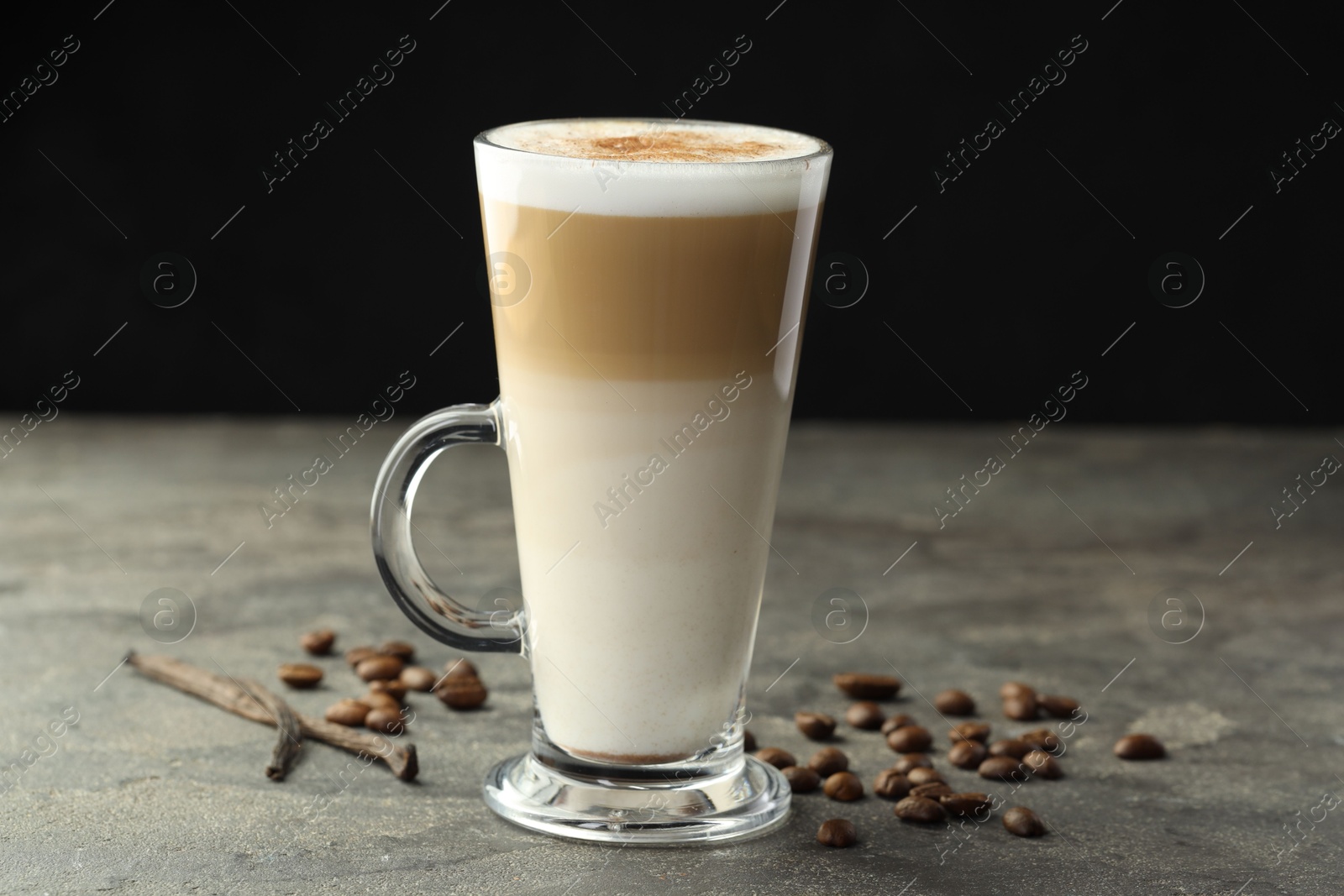 Photo of Tasty latte macchiato in glass cup, coffee beans and vanilla pods on grey table, closeup