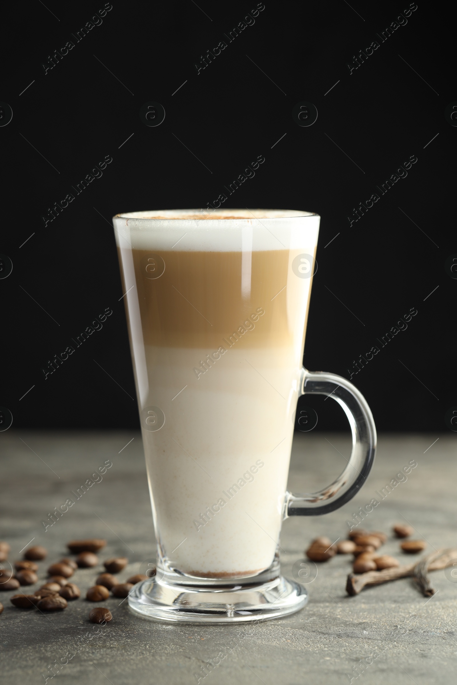 Photo of Tasty latte macchiato in glass cup, coffee beans and vanilla pods on grey table, closeup