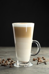 Photo of Tasty latte macchiato in glass cup, coffee beans and vanilla pods on grey table, closeup