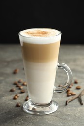 Photo of Tasty latte macchiato in glass cup, coffee beans and vanilla pods on grey table, closeup