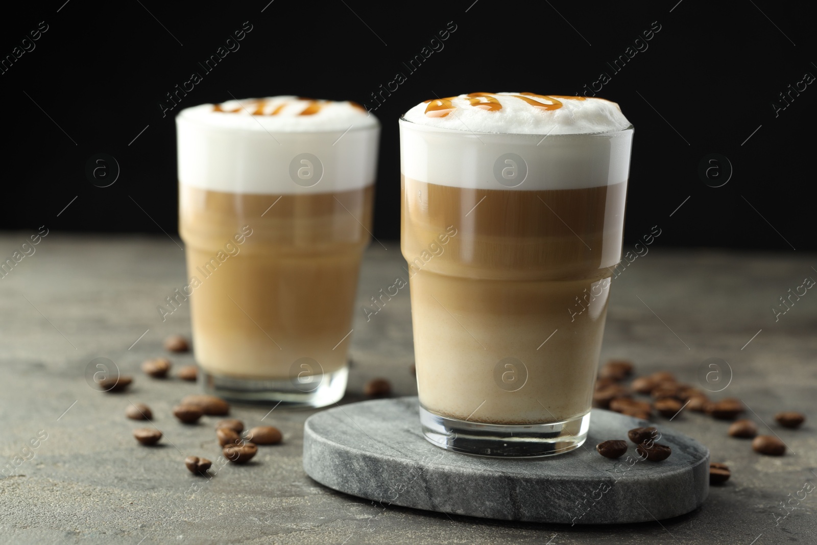 Photo of Tasty latte macchiato in glasses and coffee beans on grey table, closeup