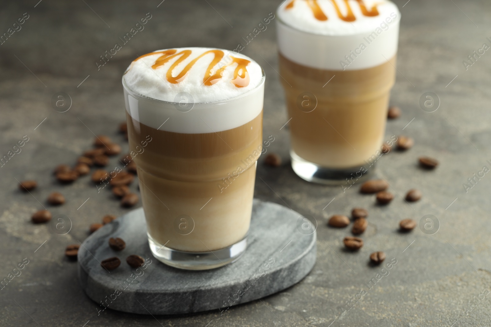 Photo of Tasty latte macchiato in glasses and coffee beans on grey table, closeup