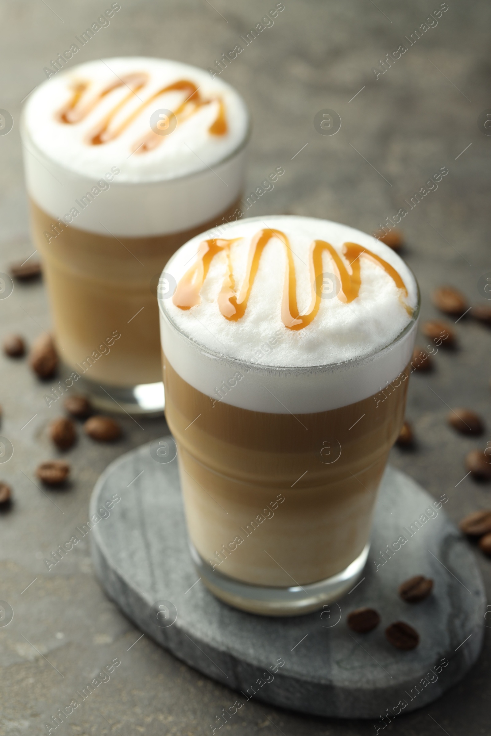 Photo of Tasty latte macchiato in glasses and coffee beans on grey table, closeup