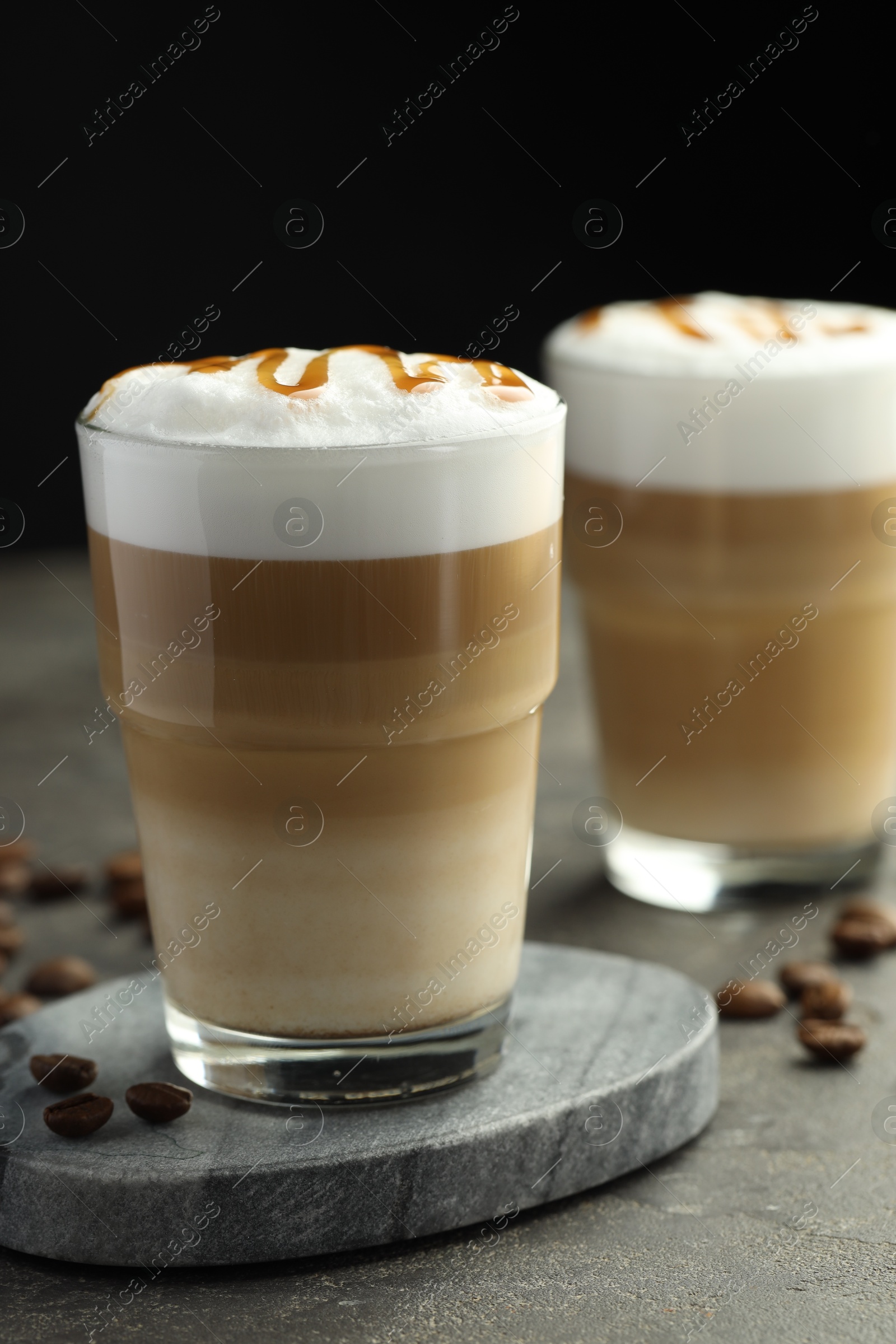 Photo of Tasty latte macchiato in glasses and coffee beans on grey table, closeup